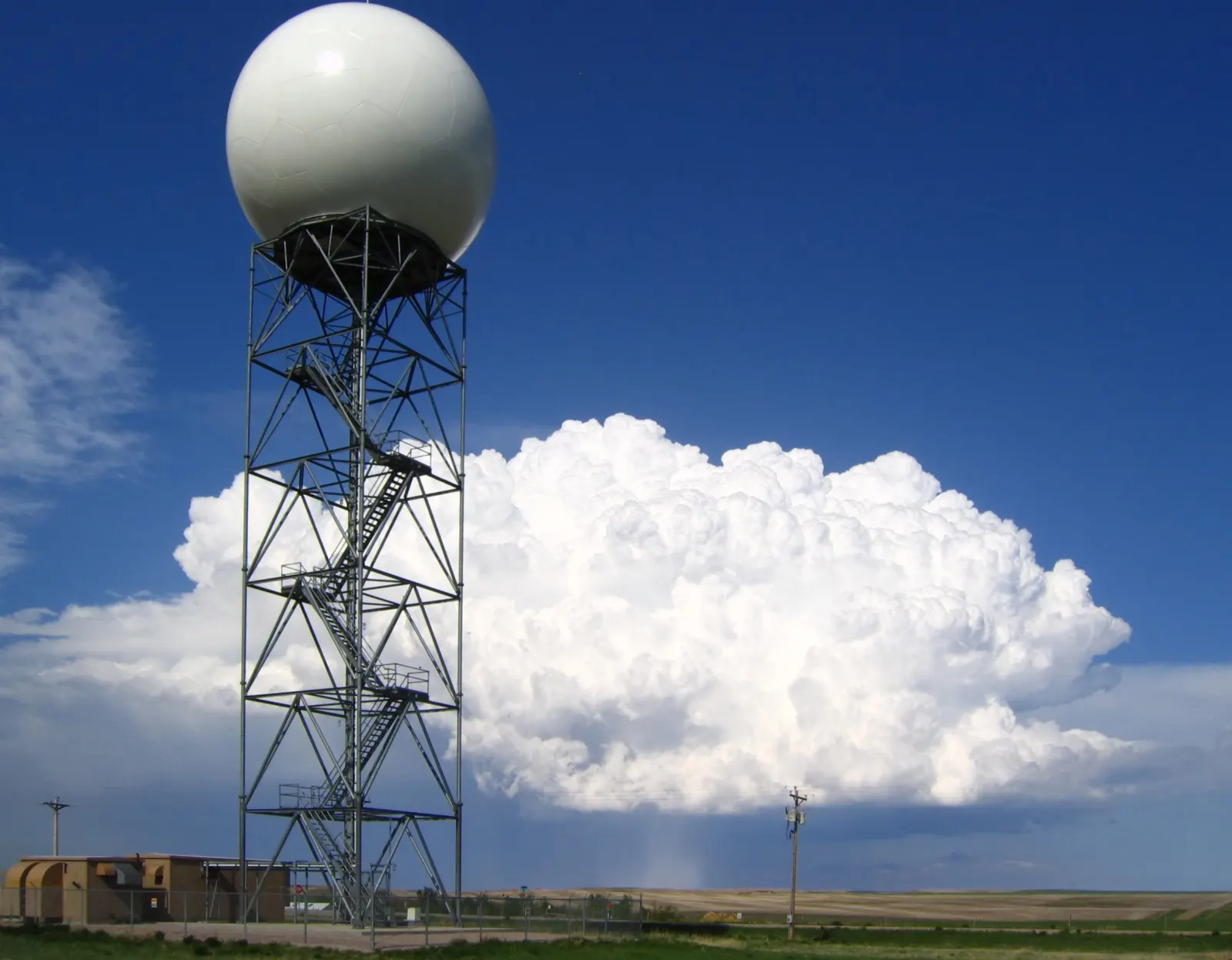 The white dome of a WSR-88D Doppler radar tower in front of a billowing storm cloud dropping hail at New Underwood, South Dakota.