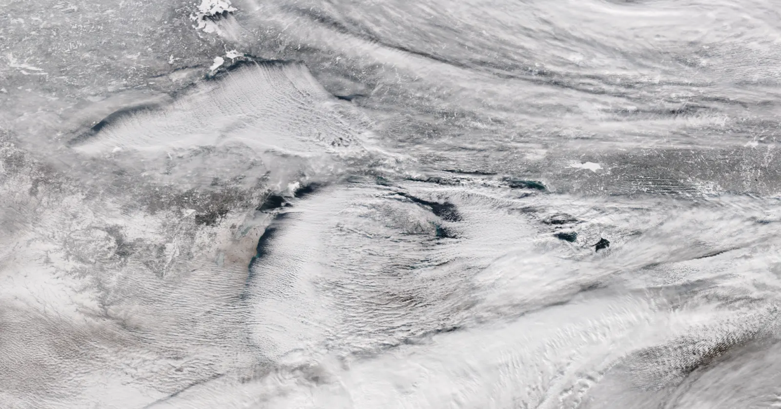 Satellite view of bands of lake-effect snow clouds streaming eastward off the Great Lakes over snow-covered ground.